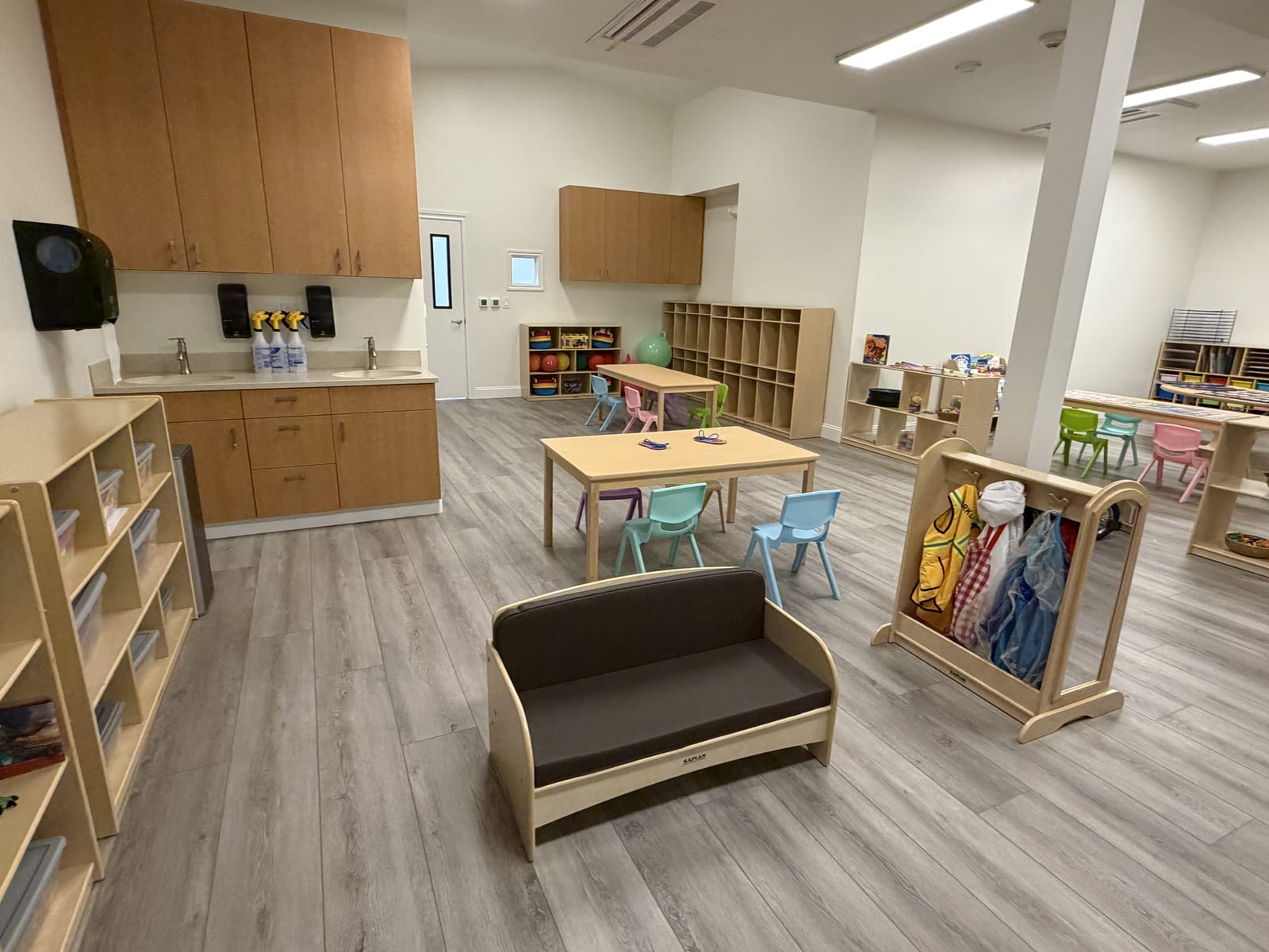 Open preschool room with a handwashing station, seating, and a dress-up rack