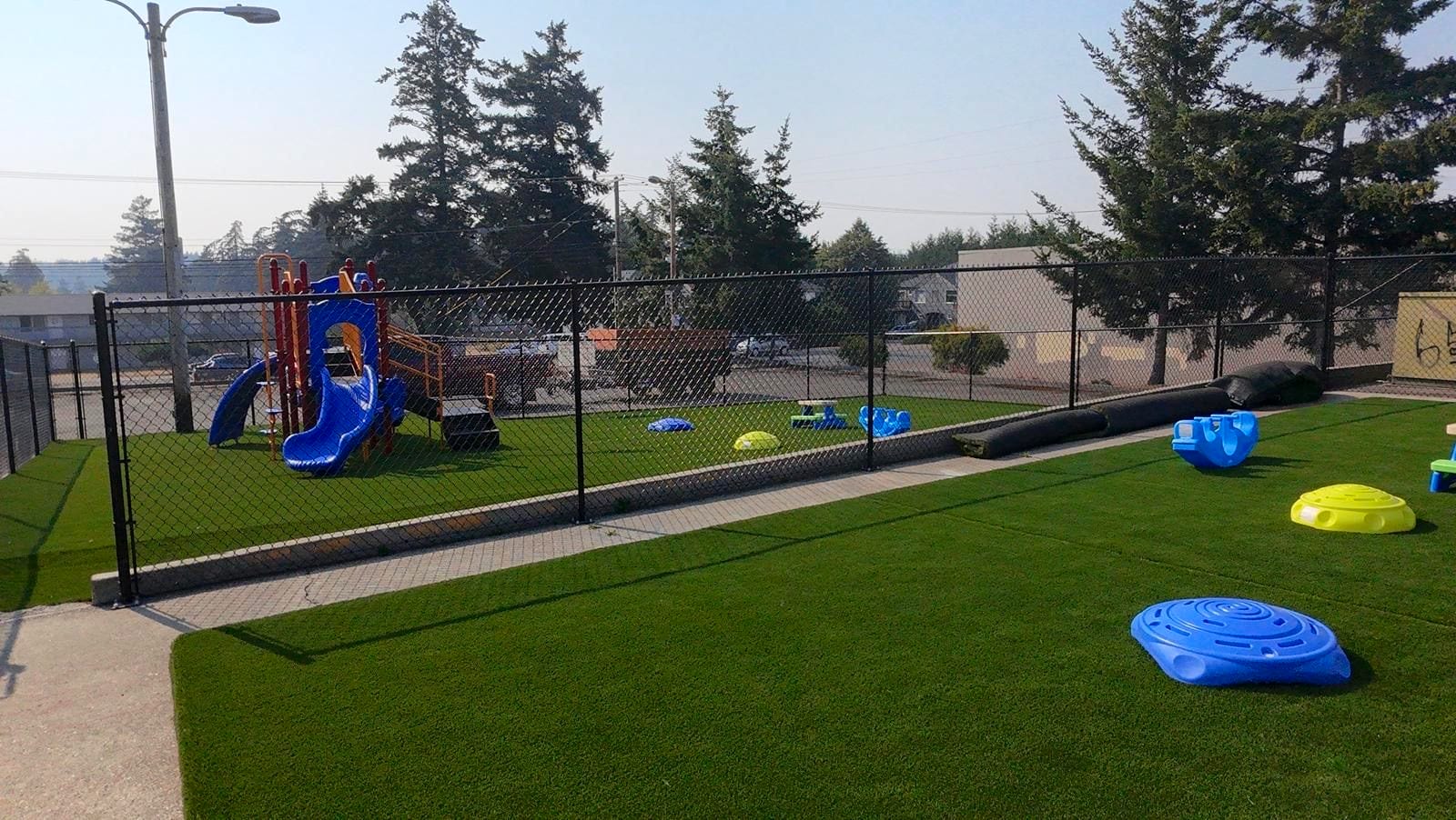 Playground structure with a slide on the fenced turf play yard at the Midway Blvd location