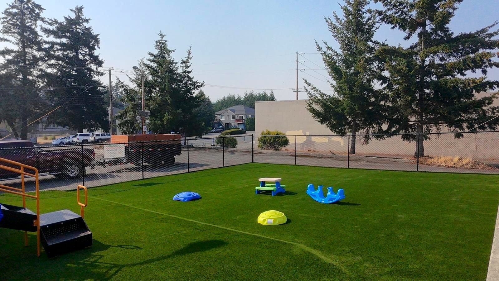 Turf play yard at the Midway Blvd location with rockers, a climber, and a picnic table set out on the grass