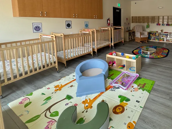 Infant room at the Midway Blvd location with a row of cribs and a padded play mat